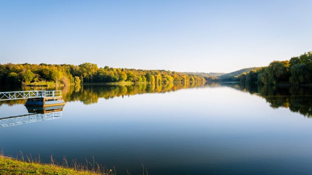 Calm waters and lush greenery reflect a tranquil scene in Pécs, Hungary.